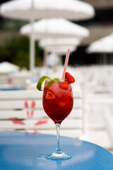 Strawberry cocktail with lemon peels, with pool in the background