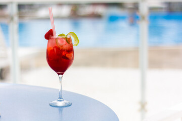 Strawberry cocktail with lemon peels, with pool in the background