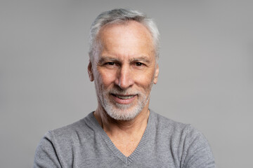 Obraz premium Closeup portrait of smiling senior man with beard and gray hair looking at camera isolated on gray background. Health care, dental concept 