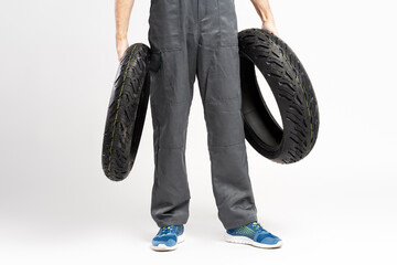 Closeup of  man holding motorcycle tire, wearing overalls isolated on gray background. Repair,...