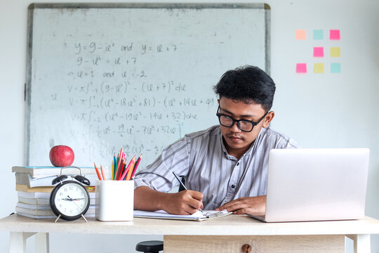 Teacher working at the classroom, writing notes on the table preparing lesson plan. 