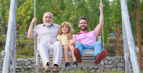 Grandfather, father and grandson child, spring banner. Men family playing on swing together Excited...