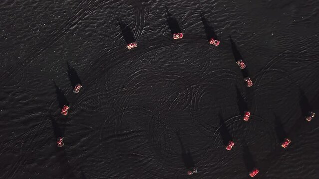 Aerial rising top view of people circling with red quad bikes on the black sand beach in Iceland, next to the ocean, on a sunny day