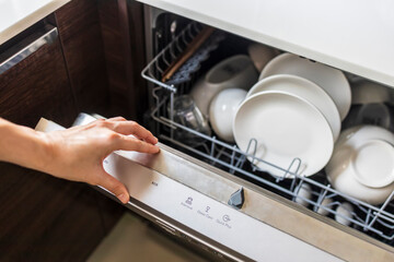 Woman fill the used dish in dishwasher machine in kitchen at home.Hand of female holding the shelf.White clean dish or bowl and cup inside the washer device.Selective focus with blur background.