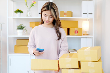 Young asian woman ,small business owner scaning product stock by mobile phone at home office
