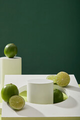 Blank minimal background with white empty podium, geometric object and fresh limes (Citrus aurantifolia) decorated on dark background. Space for product presentation with natural extracts