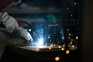 A worker's hand in a factory welding with sparks easy to use in design Up no-face - obrazy, fototapety, plakaty