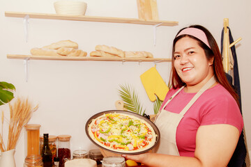 Pizza made at home : Portrait asian fat woman holding a tray of homemade pizza in the kitchen...