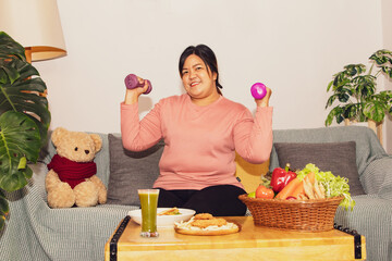Fat asian woman looking at camera in good mood sitting lifting dumbbells doing light exercise on...