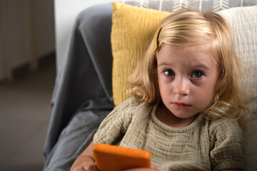 Sad girl using mobile phone sitting on sofa looking at camera. 