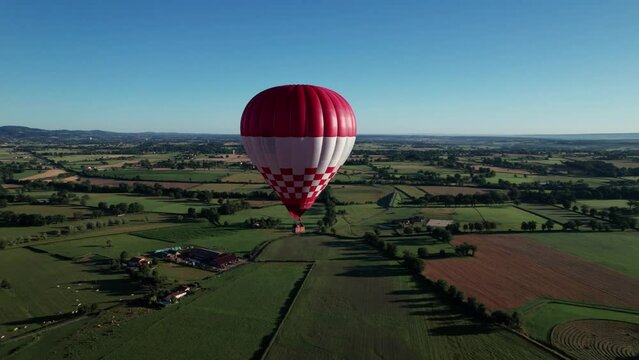 drone shot of a red and white hot-air balloon floating in the sky with the countryside in the background on a beautiful day