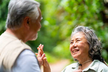 Happy Asian senior couple holding hands and walking together in tropical forest. Retired elderly people man and woman enjoy outdoor activity lifestyle travel nature hiking on summer holiday vacation.