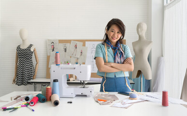 Young dressmaker with tape measure stand smiling with arms crossed. Sewing Machine and various...