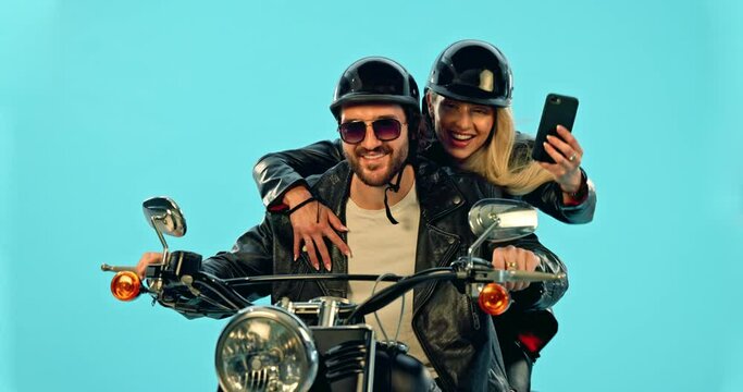 Selfie, travel and couple on motorcycle for adventure, road trip and holiday on blue background. Motorbike transport, studio and excited man and woman take picture for social media, post or memory