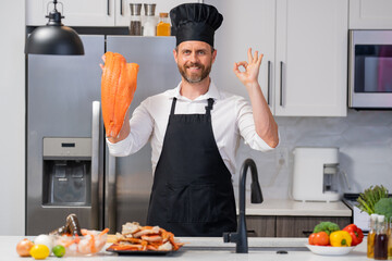 Portrait of man in chef apron and cook hat preparing fresh natural meal salmon at kitchen. Handsome...