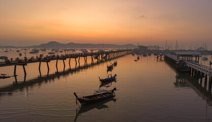 Obraz premium aerial view fishing boats on the beach at Chalong pier in sunrise..Sunrise with sweet yellow color light rays and other atmospheric effects..colorful reflection of sunrise in the sea background..d.