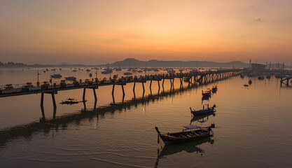 Obraz premium aerial view fishing boats on the beach at Chalong pier in sunrise..Sunrise with sweet yellow color light rays and other atmospheric effects..colorful reflection of sunrise in the sea background..d.