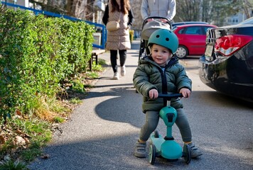 Little toddler on scooter and his parents with baby stroller walking down the street © Vedrana