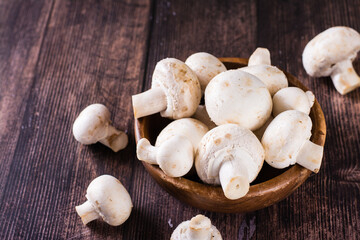 Whole fresh champignons in a plate and on a wooden table
