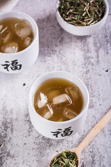 Iced green japanese hojicha tea in cups and leaves in a bowl on the table vertical view