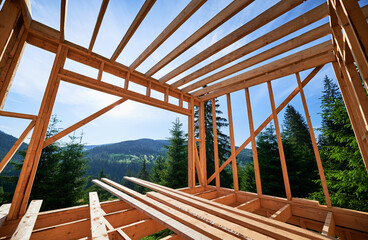 Wooden frame building under construction close to forest. Beginning of new construction of cozy house or a cottage on the edge of forested mountain area. Concept of contemporary architectural design. - obrazy, fototapety, plakaty