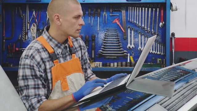 Mechanic with laptop near car engine in auto service