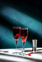 Kir Royale cocktail with black currant liqueur, prosecco wine and red cocktail cherry. Dark green background, hard light and shadow pattern