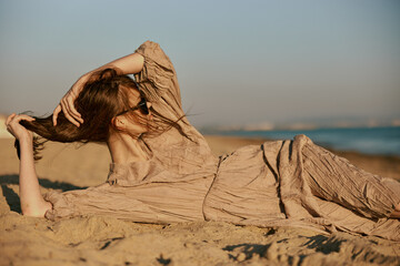 a woman in black sunglasses lies on the sand in a dress and straightens her hair