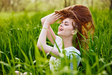 portrait of a beautiful woman sitting in tall grass and holding her long hair