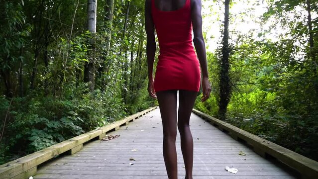 Black sexy woman wears sensual short red dress. Modeling session in a park. Very thin model, walks on the catwalk in a park. His skin is black and she has an afro.