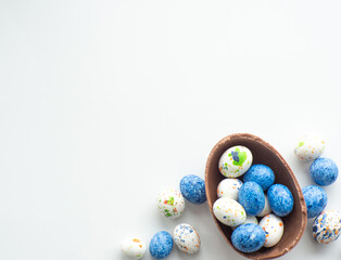 Sweet Easter concept. Blue, white and chocolate easter eggs with sweet dragee on white background with copy space. Design for a greeting card for the Easter holiday. Flat lay. Preparation for holiday.