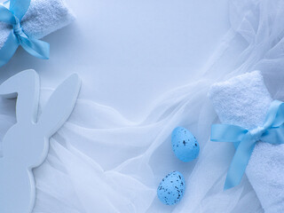 Wellness Easter concept. Set white towels tied with a ribbon in a bow, blue eggs, bunny and copy space. White Easter card. Rolled towels in spa salon. Hygiene and spa, relaxation as gift for holidays.