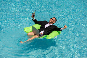 Excited business man floating in suit drink summer cocktail and using laptop in pool. Travel business. Office employee using laptop in pool on summer day. Successful businessman dreams in summer pool.