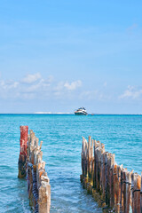 large yacht on the caribbean beaches of cancun Mexico. blue sky with lots of clouds and old wood in foreground out of focus.