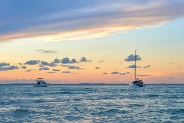 Fototapeta na wymiar 2 yachts at sunset on north beach isla mujeres. shades of blue and orange in the sky full of clouds. riviera maya beaches.