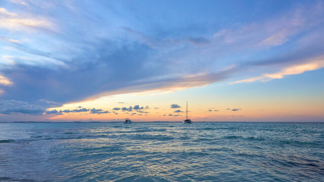 2 yachts at sunset on north beach isla mujeres. blue and orange tones in the sky full of clouds. mexican caribbean beaches. landscape photography.