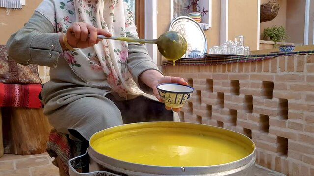 Wide view of a Persian Iranian woman serving sweet juicy dessert in Ramadan wear Muslim hijab in a local house with traditional architecture brick pattern in the backyard in Ardakan Yazd