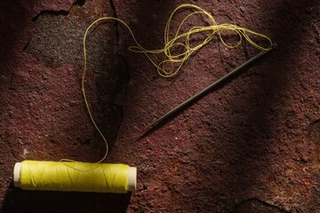 Spool of yellow thread and .needle on a dark metal background