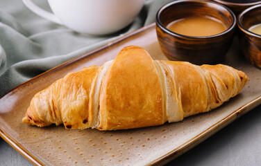 Fresh french croissants with chocolate on plate, honey, and tea
