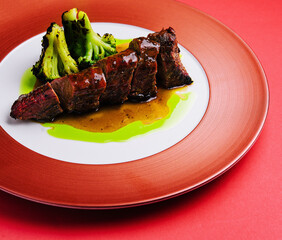 Roasted pork with sauce and broccoli on red plate