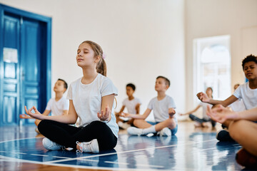 Schoolgirl and her classmates meditating while exercising Yoga on physical education class.