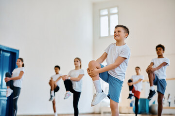 Happy schoolboy stretching his leg while having physical education class with his classmates.