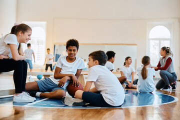 Fototapeta na wymiar Happy black boy talks to his friends during physical activity class at school gym.