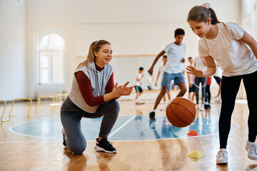 Schoolgirl leading basketball among cones while sports teacher is supporting her during physical...