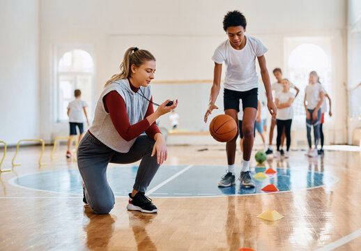 Young female coach using stopwatch during physical activity class with school kids. - Powered by Adobe