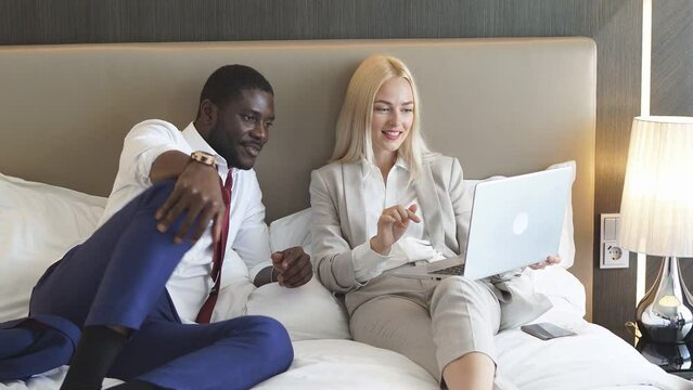 Happy family in business clothes is lying on bed in hotel using laptop. Beautiful couple in hotel.