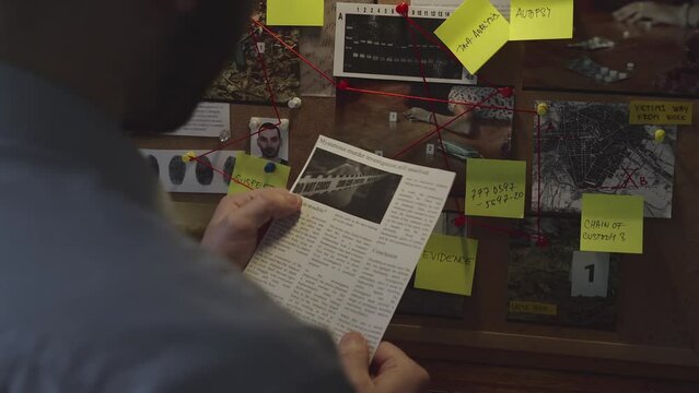 Detective standing in front of an investigation board reads about the investigation from a newspaper clipping