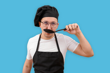 A male chef is tasting food from a spoon on a blue background. Cooking and people concept