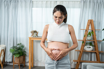 Pregnant teenage mom stands in living room and hands form heart shape on belly. express love waiting for her unborn child A pregnant woman stood motionless in the middle of the room.