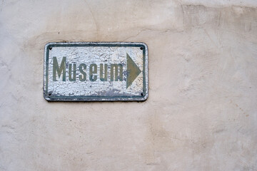 Fototapeta premium Yellowed and weathered sign full of cracked paint with a directional label saying MUSEUM painted on it.